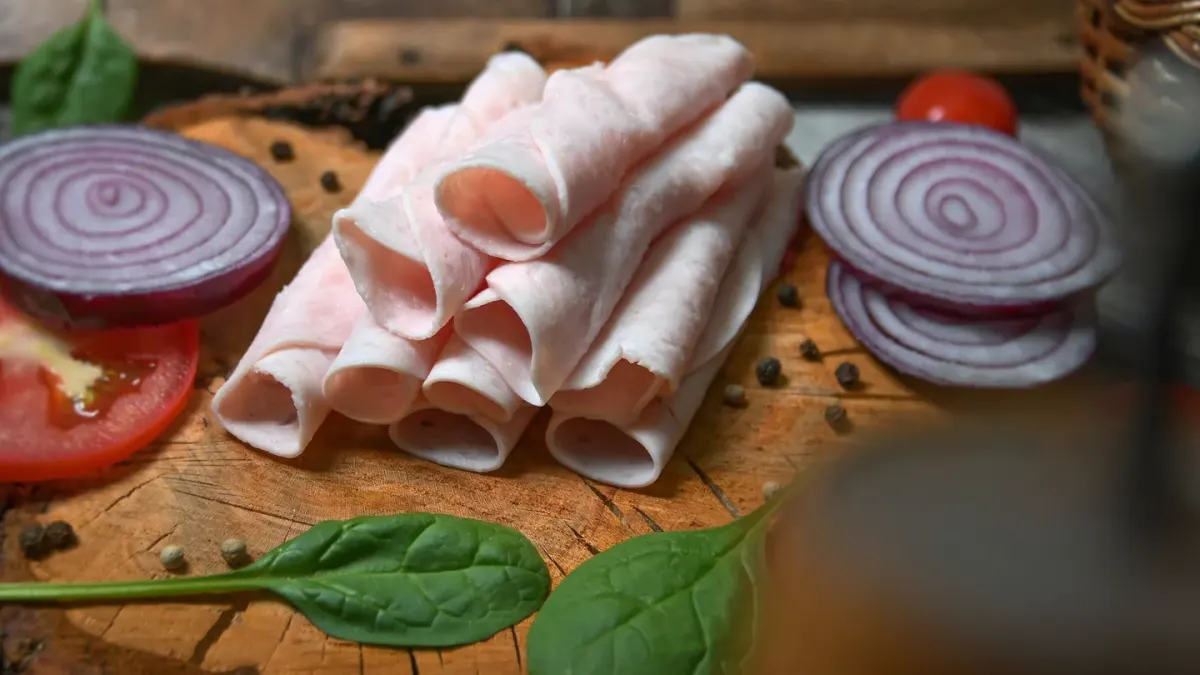 A dog looking up at a plate of sliced ham on a kitchen counter