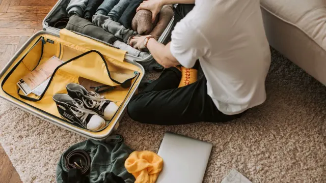 A dog stretched out on a hotel room floor beside an open suitcase