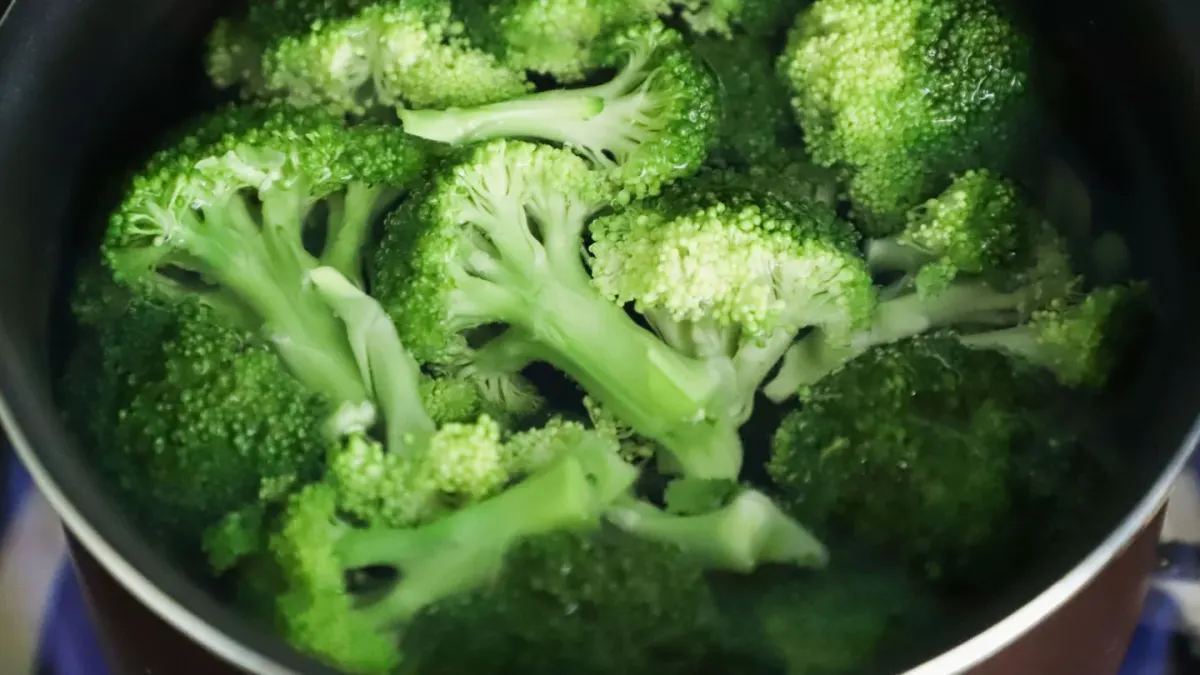 A small bowl of plain steamed broccoli florets sitting beside an empty dog bowl on a kitchen floor