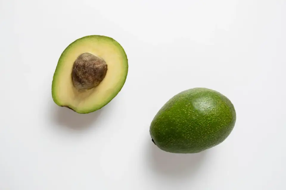 An avocado pit sitting beside two avocado halves on a wooden cutting board
