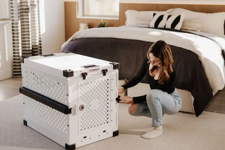 An owner kneeling beside a crate to calm a whining puppy