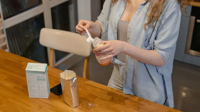 An owner spooning a scoop of powder over a dog's food bowl in a kitchen